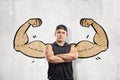 Close up front view of young athletic man with arms crossed, standing against wall with drawing of big muscular arms Royalty Free Stock Photo