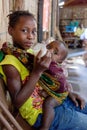 Close up front view of a young unidentified African girl feeding her baby brother