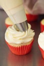 Close up frosting being applied to a vanilla cupcake