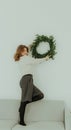 Close up fun cool smiling young girl with Christmas wreath on workspace area isolated on plain light background New Year