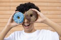 Close-up of a funny African-American man making face and eyes out of chocolate and blue donuts Royalty Free Stock Photo