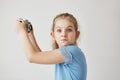 Close up of funny blonde girl in blue shirt holding camera in hands,going to make selfie when her friend starts to