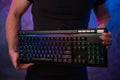 Close-up on gamer`s hands holding a keyboard. Background is lit with neon lights