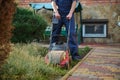 Close-up gardener in work uniform, mowing backyard grass, moving after a push electric lawn mower. Landscaping concept