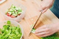 Close-up of gentle female hands slice on the wooden board the stalks of green onions making salad. The concept of a