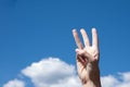 Close-up gesture of a woman`s hand showing three fingers isolated on a background of blue sky with clouds Royalty Free Stock Photo