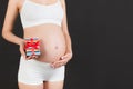 Close up of gift box in pregnant woman`s hands against her abdomen at black background. Young mother in white underwear. Happy Royalty Free Stock Photo