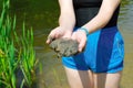 A girl in blue shorts holds river mud in her hands against a background of green river thickets Royalty Free Stock Photo