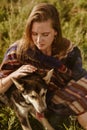 close-up. Girl in ethno cape with natural beauty without makeup strokes the dog& x27;s hand sitting in the grass Royalty Free Stock Photo