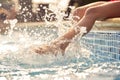 Close Up Of Girl Having Fun Splashing Feet Sitting On Edge Of Swimming Pool On Summer Vacation