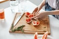 Close up of girl`s hands sliced grapefruit knife and rosemary on wooden desk. Copy space. Royalty Free Stock Photo