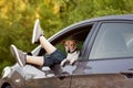 Close-up of the girl`s legs sticking out of the car window, next to the window looks out a dog. A trip, a walk, a trip. Friend, Royalty Free Stock Photo