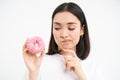 Close up of girl thinks of braking her diet, looking at tempting glazed doughnut, white background