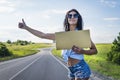 Close up girl travels hitchhiking with a cardboard sign in her hands. a girl in glasses shorts and heels road on Royalty Free Stock Photo