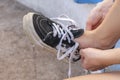 Close-up of a girl tying white shoelaces on black sneakers. Untied shoelaces