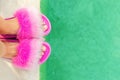 Close-up girl or woman feet in glamour fashion fluffy slippers standing on edge of pool with clear turquoise water. Legs wearing Royalty Free Stock Photo