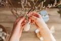 Close-up of a girl's hands hanging a decorative Easter egg on a willow branch at home. Decorating your home for