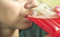 Close up of girls face and lips drinking strawberry red juice from the glass as refreshment, real people, selective focus