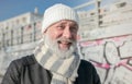 Close up of gladsome bearded man wearing white knitted hat and scarf on urban background