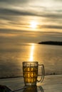 Close up a Glass of beer is standing on a table with blurred sea on background. Beer with foam. Sunset and natural. Alcohol and Royalty Free Stock Photo