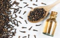 Close up glass bottle of clove oil and cloves in wooden spoon on white rustic table