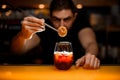 close-up of glass with cold drink and male hand accurate holding dry slice of orange with tweezers over it Royalty Free Stock Photo