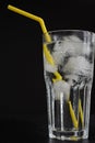 Close-up of glass cup with water, many ice cubes and yellow straw on black background Royalty Free Stock Photo