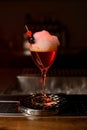 Close-up of glass with foamy cocktail decorated with red berry and small heart on the bar