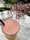 Close-up of a glass of freshly squeezed juice and a vase of pink miniature flowers on a table at an outdoor cafe Royalty Free Stock Photo