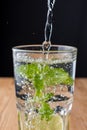 Close-up of glass full of water with lemon and mint, with water falling, on wooden table and black background in vertical, Royalty Free Stock Photo