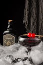 Close-up of glass of Halloween black widow cocktail with red cherries, spiders and dark bottle on spider web, black background Royalty Free Stock Photo