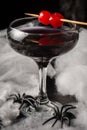 Close-up of glass of Halloween black widow cocktail with red cherries and spiders on spider web, black background, Royalty Free Stock Photo