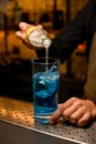 Close-up of glass with ice cubes and blue beverage into which bartender accurate pours drink from bottle Royalty Free Stock Photo