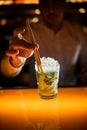 close-up of glass with iced mojito and hand of bartender inserts drinking straw in glass