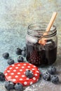 Close-up of glass jar with blueberry jam and wooden spoon, on blue background with blueberries and polka dot lid, selective focus Royalty Free Stock Photo