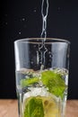 Close-up of glass with mint and lemon with water falling on wooden table and black background, vertical Royalty Free Stock Photo