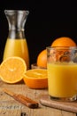 Close-up of glass with orange juice, bottle, knife, unfocused oranges on wooden table, black background, vertical Royalty Free Stock Photo