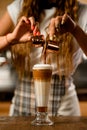 Close-up of glass with syrup and whipped cream into which barista carefully pours espresso