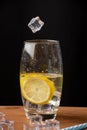 Close-up of glass with tonic water with ice and lemon with an ice falling, on wooden table and black background, Royalty Free Stock Photo