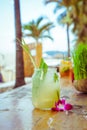 Close up of glass with tropical refreshing lemongrass coctail with mint, lime and flower decoration on palm beach