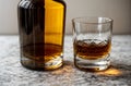 close up of glass of whiskey and whisky bottle without etiquette on marble table