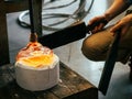 Close up of a glassblower artisan shaping the hot molten glass at strong fire inside a workshop