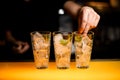 close-up of glasses with ice cubes in which hand of bartender puts cucumber slices