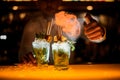close-up on glasses with iced mojito cocktail on which hand of bartender splashes and sets fire