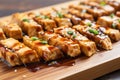 close up of glazed teriyaki tofu slices on wooden board