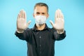 Close-up of the gloved hands of a young man in a medical protective mask on a blue background. Social distance. Stop gesture