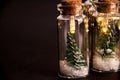 Close up of glowing lights decoration of glass jars with corks inside which there are small green Christmas trees on artificial