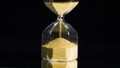 Close-up of golden hourglass. Stock footage. Stylish hexagon hourglass with falling gold specks on black isolated