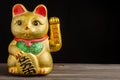 Close-up of golden lucky cat with green and red tones, on dark wooden table, black background, Royalty Free Stock Photo