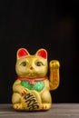 Close-up of golden maneki neko on wooden table and black background, vertical